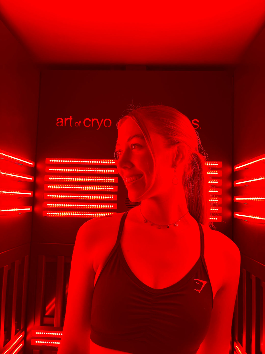 Junge Frau steht in Kabine für Lichttherapie Wärmetherapie, lächelt und genießt LED-Rotlichttherapie